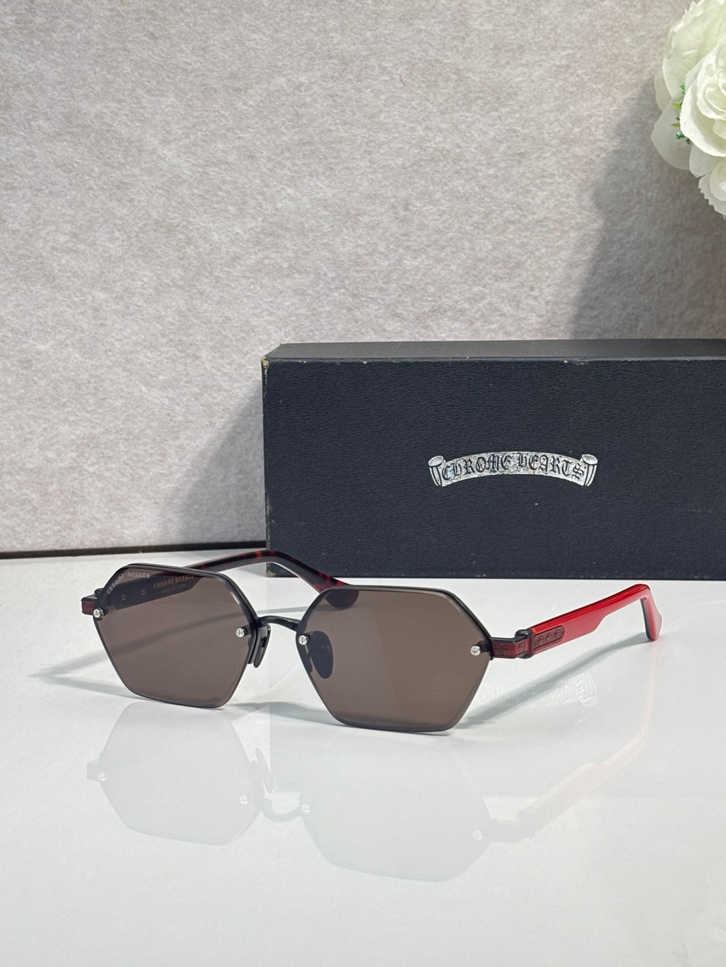 Hexagon sunglasses with dark lenses, brown frame, and red temples with gold hardware