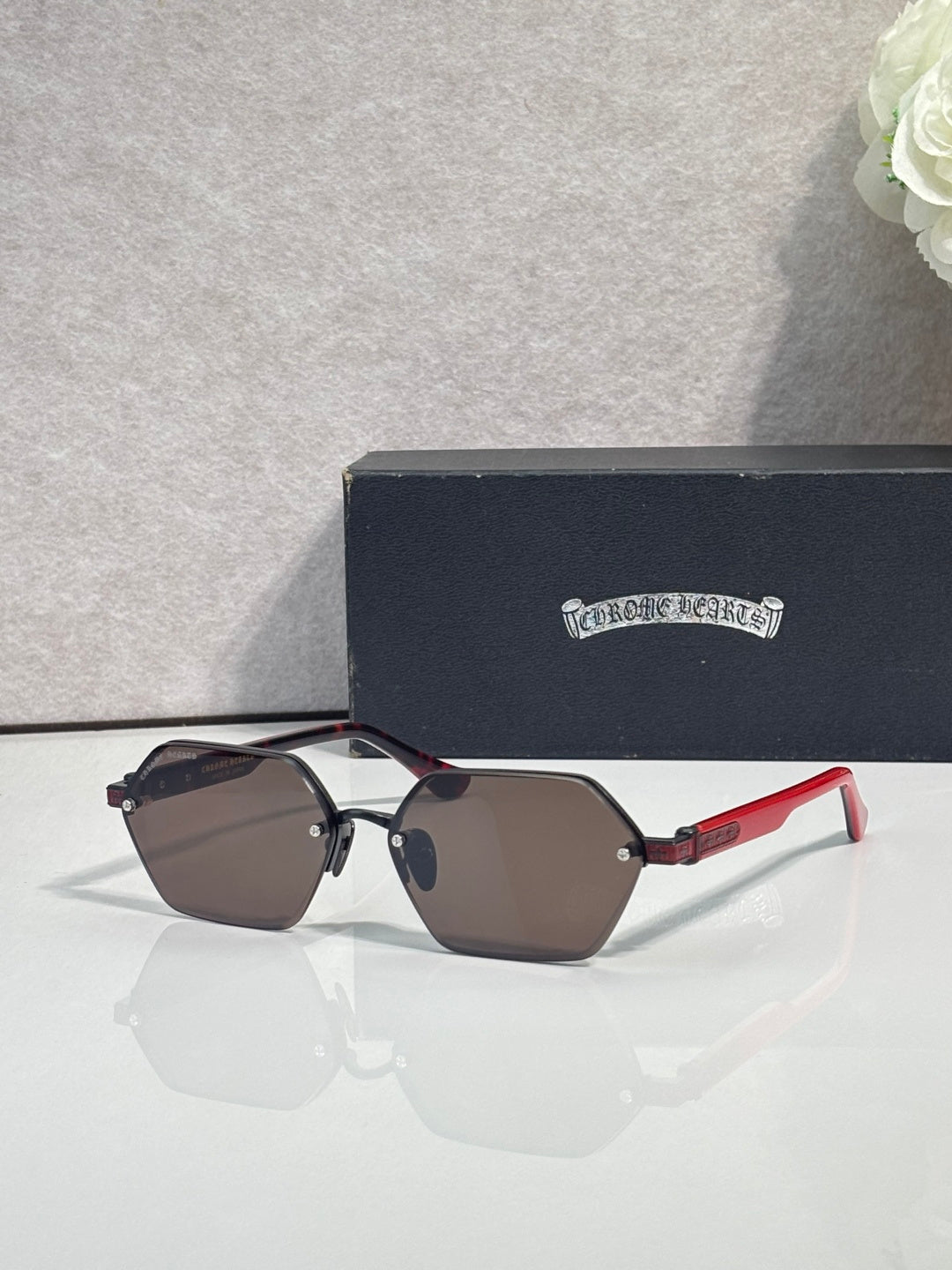 Hexagon sunglasses with dark lenses, brown frame, and red temples with gold hardware