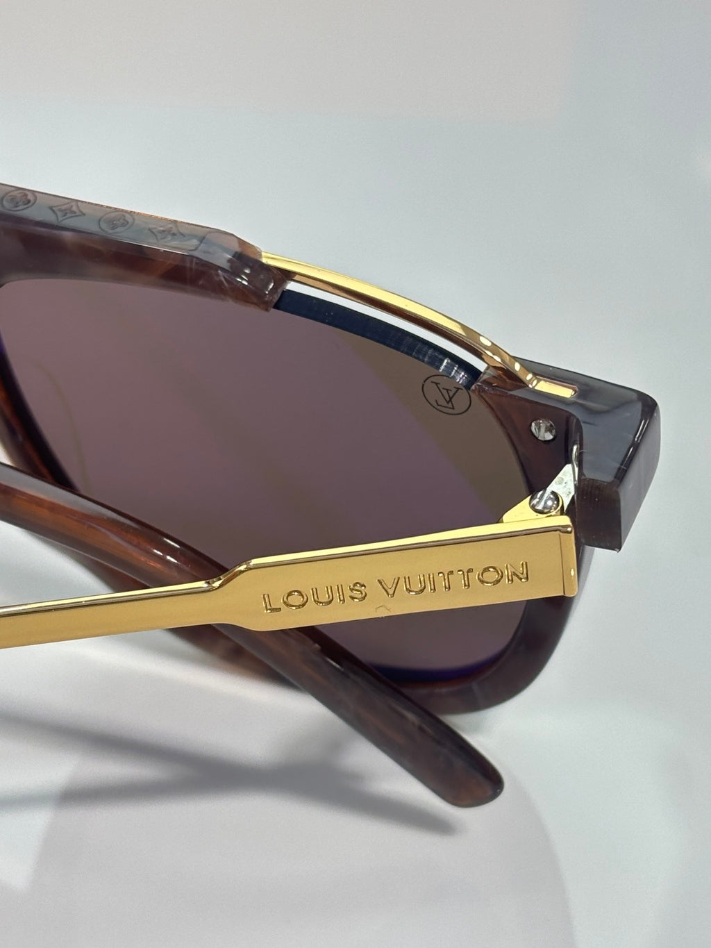 Louis Vuitton sunglasses close-up with dark lens, gold arm trim, and frame logo