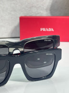Prada glasses close-up with glossy black frame and dark oval lenses, red case behind