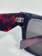 Prada glasses close-up of hinge with silver logo hardware on dark frame