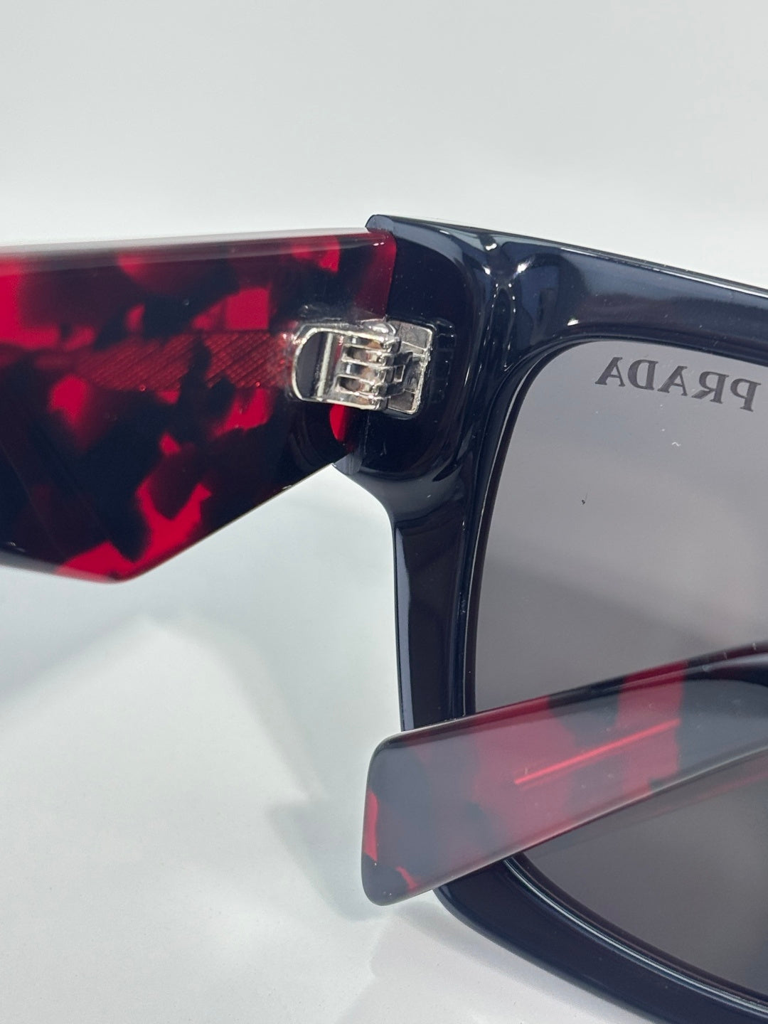 Prada glasses close-up of hinge with silver logo hardware on dark frame