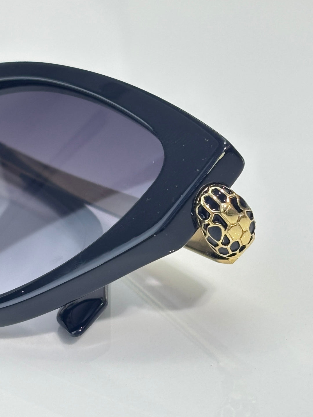 Close-up of dark navy cat-eye sunglasses with gold serpent-style temple detail, tinted lens