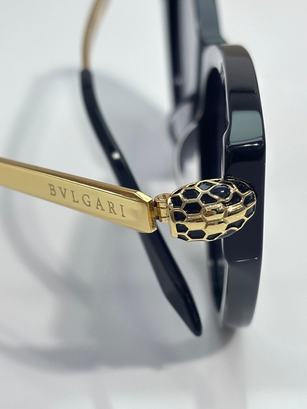 Gold temple bar and detailed gold clasp on dark navy cat-eye sunglasses, tinted lenses