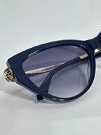 Cat-eye sunglasses with dark navy frames and gold clasp on the temple, tinted lenses