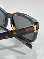 Tortoise eyeglass arm with gold emblem, dark lenses, close side view