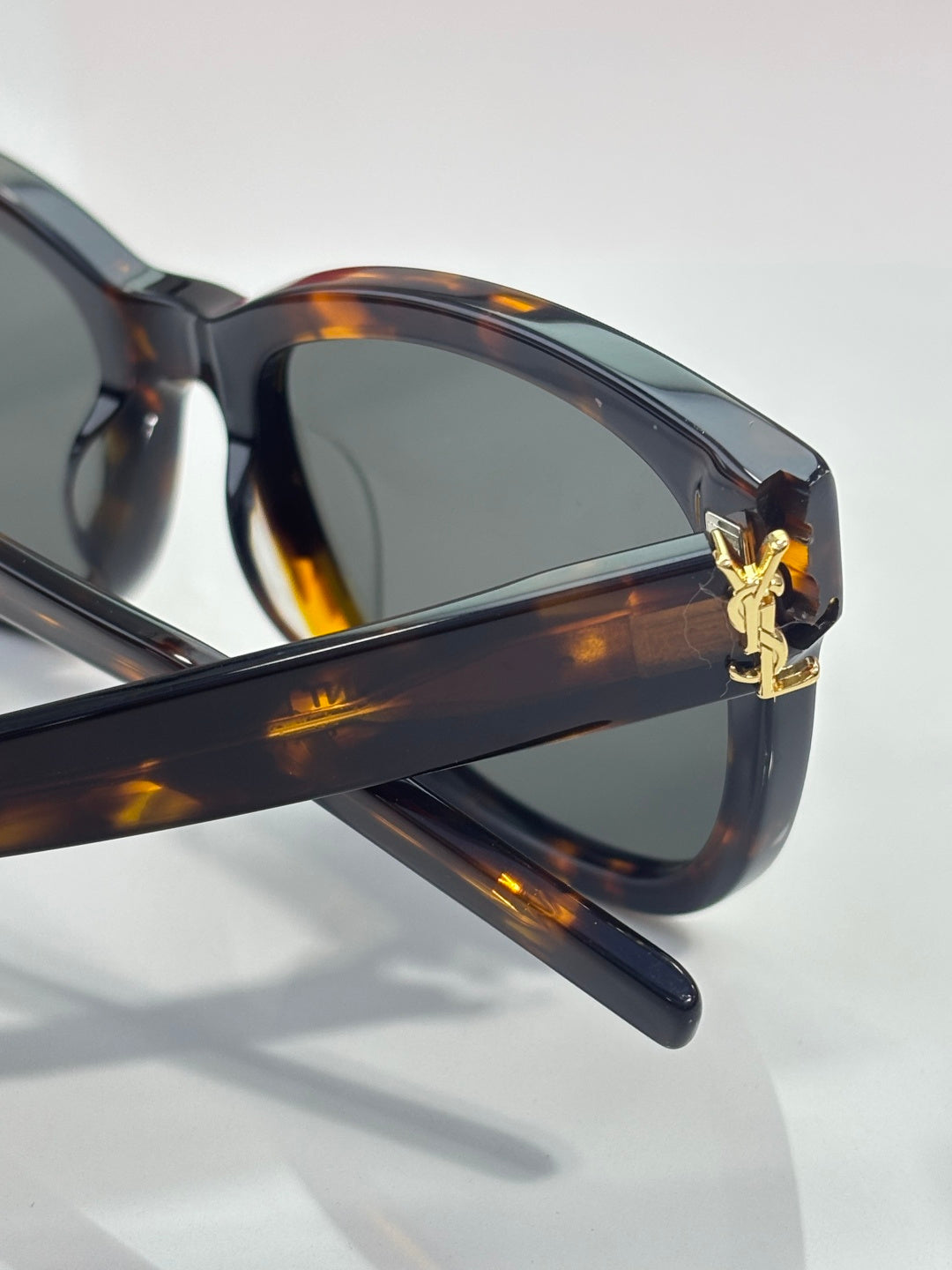 Tortoise eyeglass arm with gold emblem, dark lenses, close side view