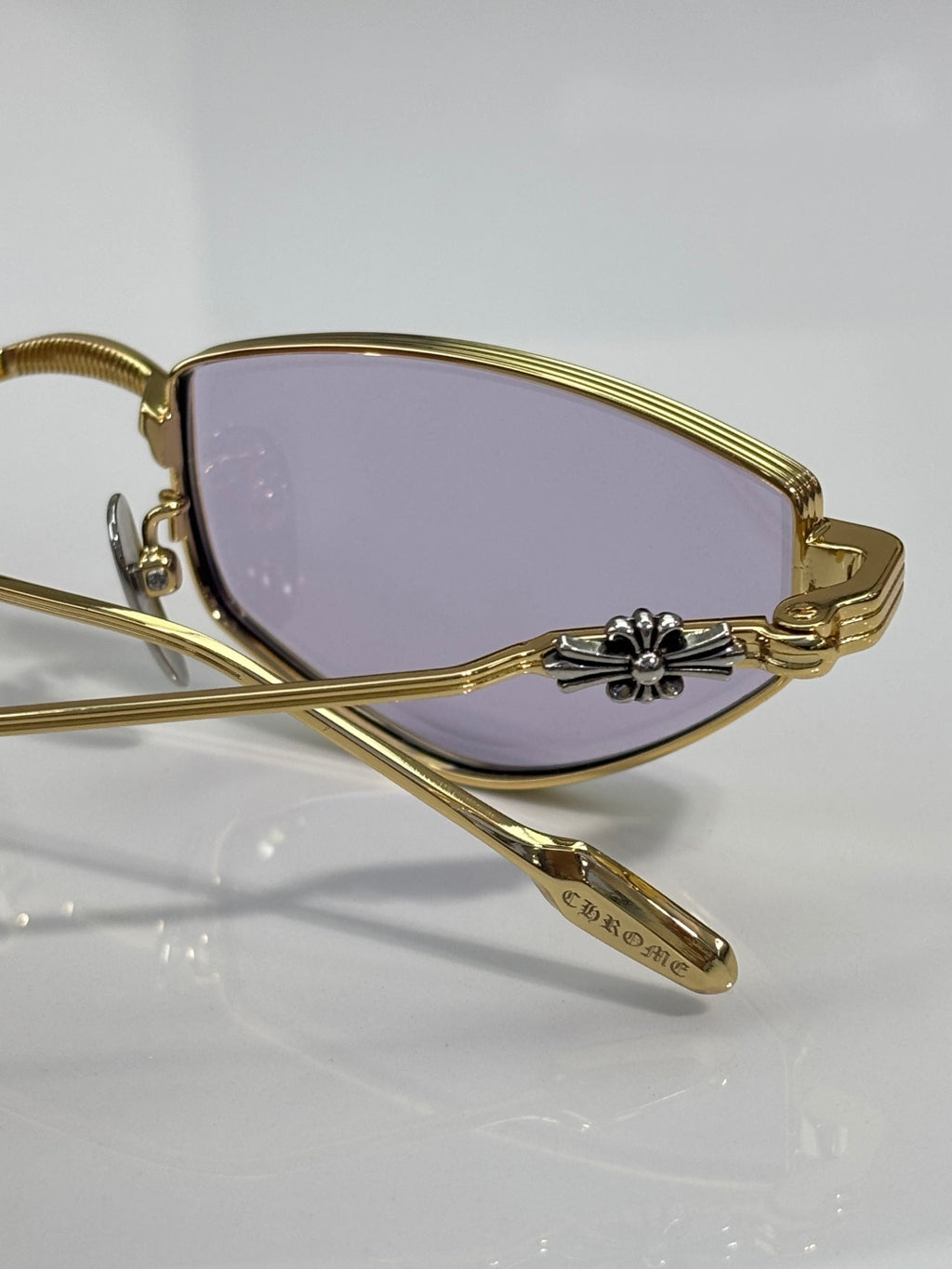 Close-up of gold metal glasses with purple-tinted lens and engraved temple