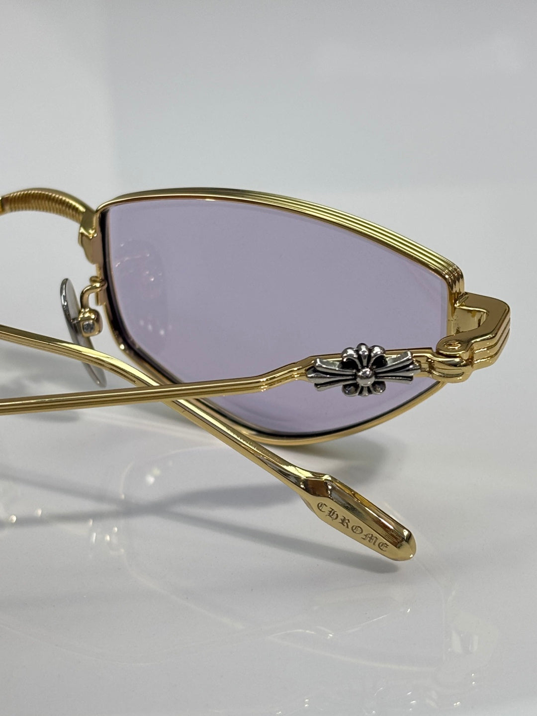 Close-up of gold metal glasses with purple-tinted lens and engraved temple