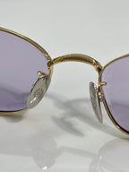 Gold eyeglass hinge with oval charm on temple and purple-tinted lens edge