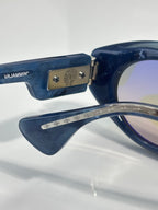 Close-up of navy glasses with VAJAMMIN' text on the temple and metal emblem