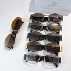 Assorted cat-eye sunglasses set with dark lenses and gold-tone frames, stacked on a box.
