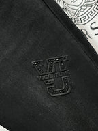Black Versace jeans with small studded logo patch on the thigh