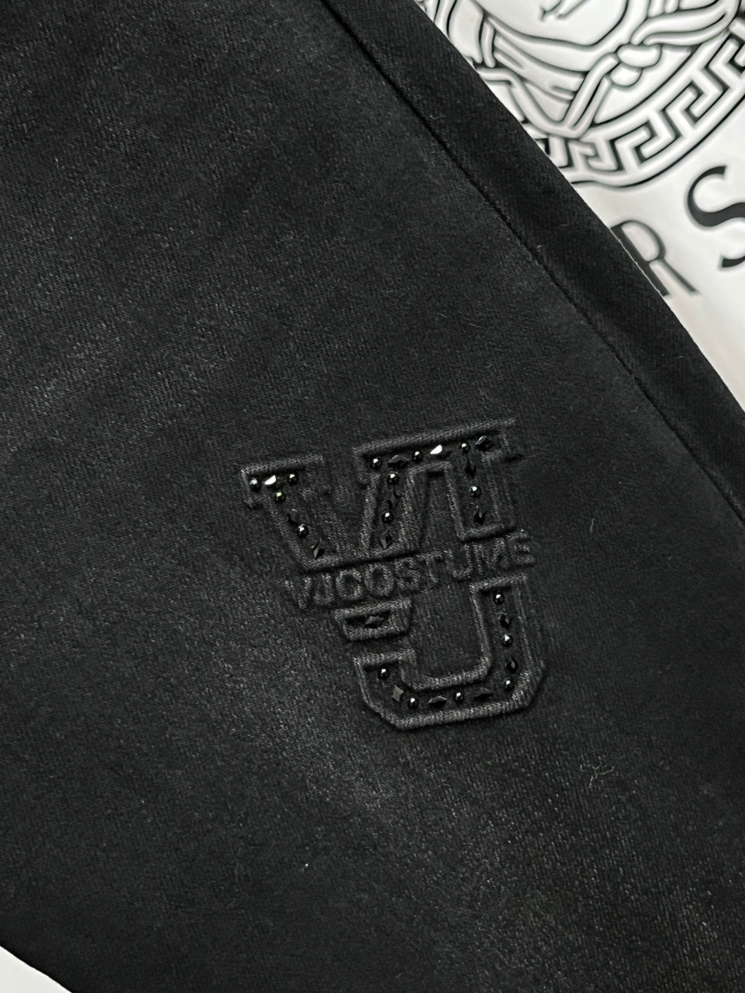 Black Versace jeans with small studded logo patch on the thigh