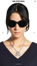 Balenciaga pendant necklace with silver chain and charm clover design worn with sunglasses