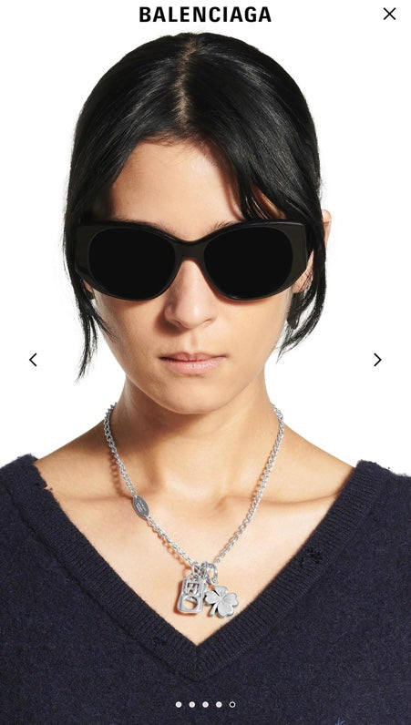 Balenciaga pendant necklace with silver chain and charm clover design worn with sunglasses