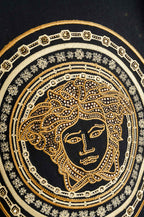 Close-up of gold Medusa-style emblem on black T-shirt