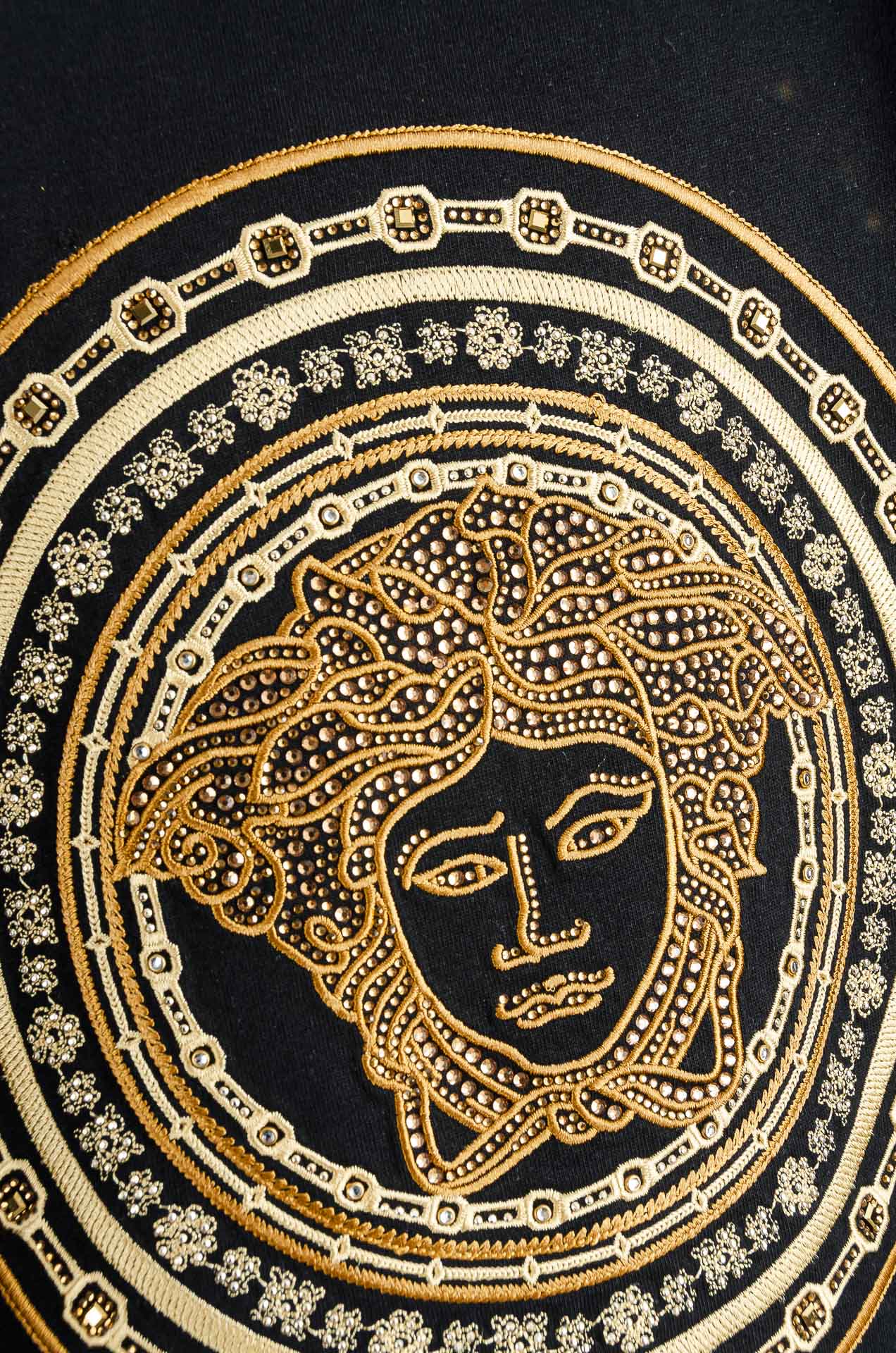 Close-up of gold Medusa-style emblem on black T-shirt