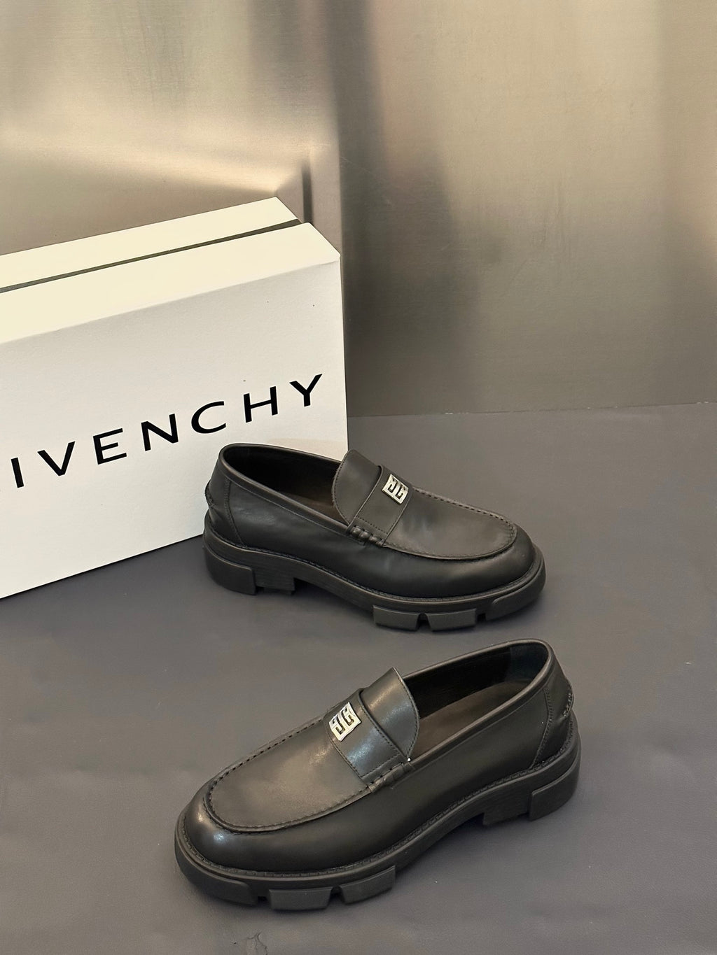 Two dark leather loafers with square logo buckle strap and ridged platform sole