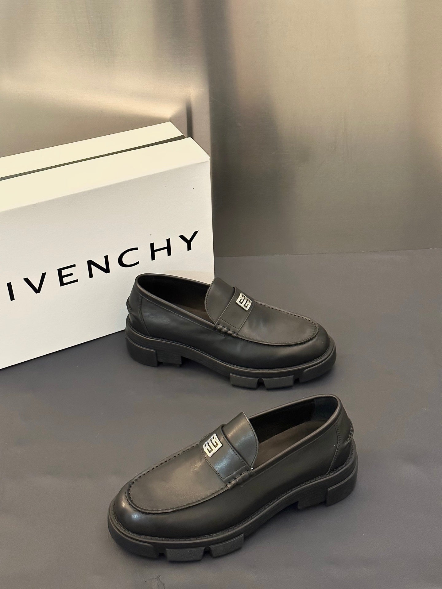 Two dark leather loafers with square logo buckle strap and ridged platform sole
