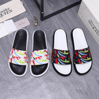 Black slide sandals with white sole and multicolor graffiti-style band across top.