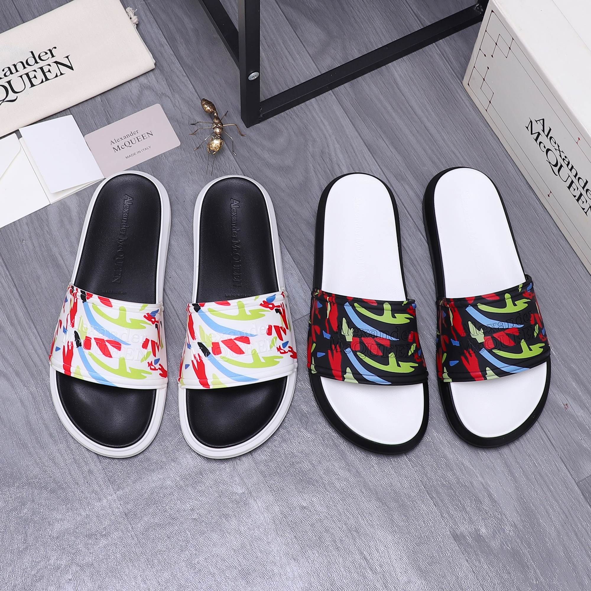 Black slide sandals with white sole and multicolor graffiti-style band across top.