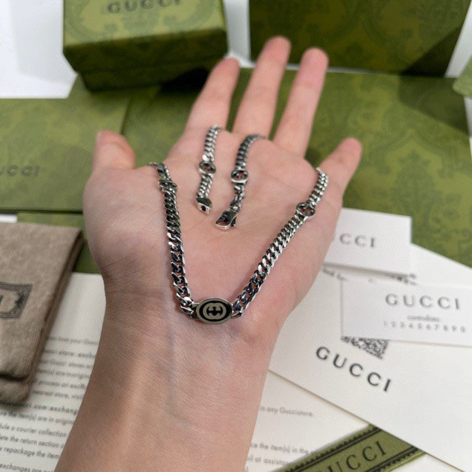 Silver-tone chain necklace on open hand, round logo pendant at center