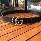 Black leather belt with gold-tone ornate buckle on wooden surface