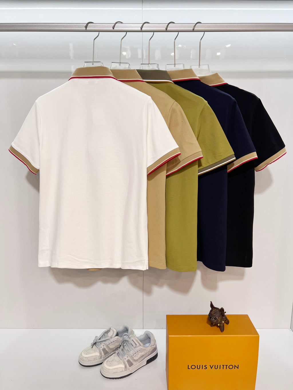 Short-sleeve polo shirt backs on hangers in white, olive, and navy with red-trim cuffs.