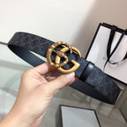 Gucci belt with dark monogram strap and gold double-G buckle, held up