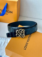 Dark navy croc belt with gold-tone interlaced buckle, on orange box