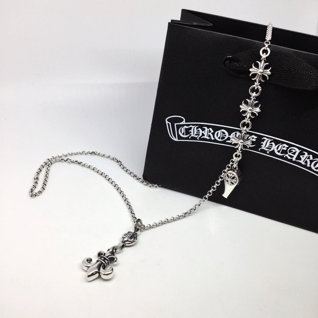 Silver chain necklace with fleur-de-lis and charm dangles, on black pouch