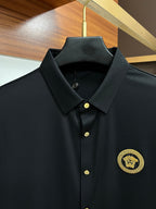 Dark button-up shirt close-up with point collar, gold buttons, and gold emblem