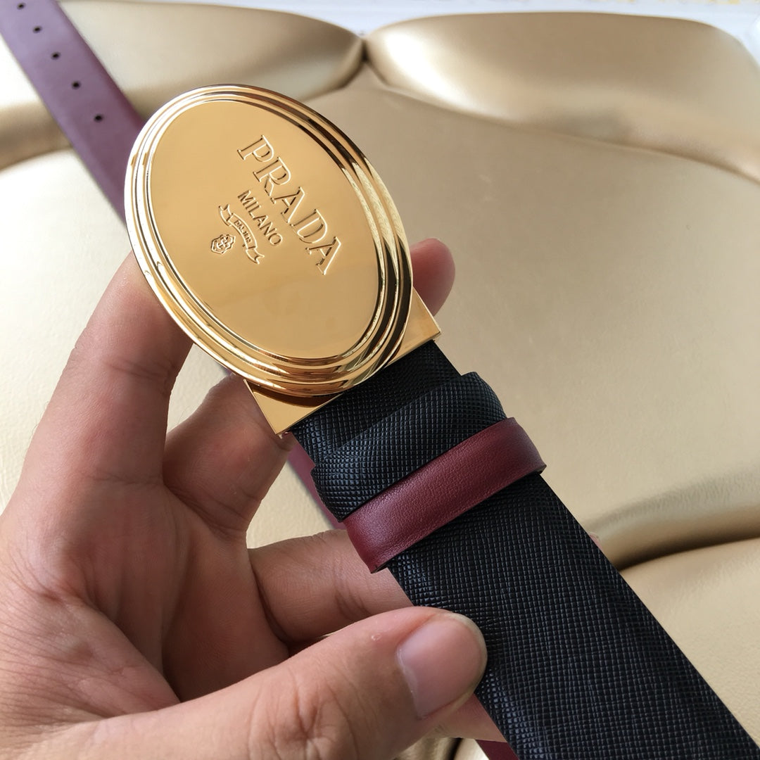 Designer belt close-up: oval gold logo buckle on navy textured strap with burgundy edge
