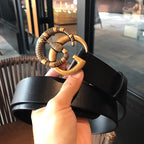 Black leather belt with gold-tone buckle detail held in hand