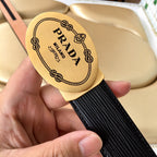 Prada belt logo plate close-up on black textured strap with tan strap edge.