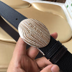 Prada belt close-up of oval silver logo plate on dark textured leather strap