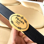 Prada belt close-up of gold oval logo buckle on textured dark blue strap.