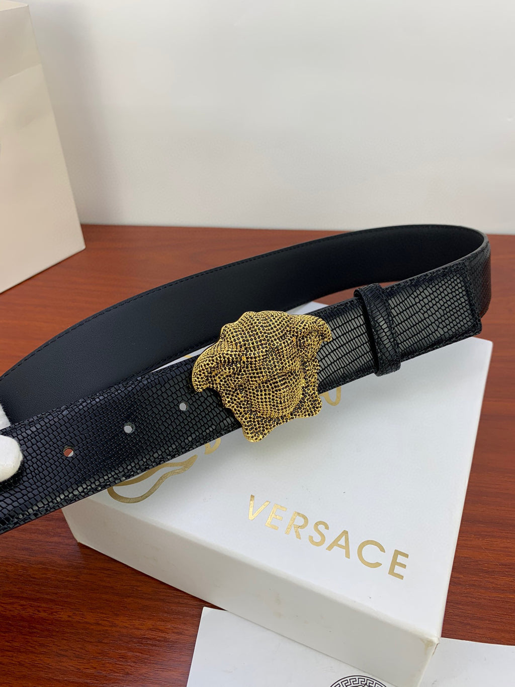 Black embossed belt with gold Medusa-style buckle centered on the strap.