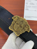 Black embossed belt with gold textured Medusa-style buckle in close view.