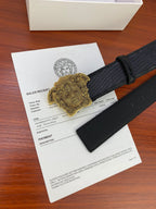 Black embossed belt with gold Medusa-style buckle and dark strap end.