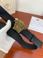 Black leather belt with gold Medusa-style buckle and arched profile.