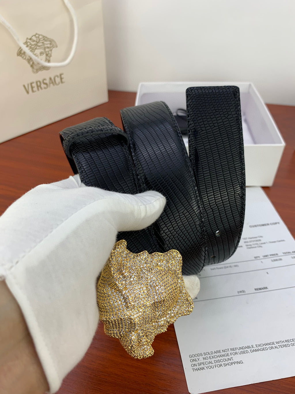 Black textured belt with gold emblem buckle, held near a receipt
