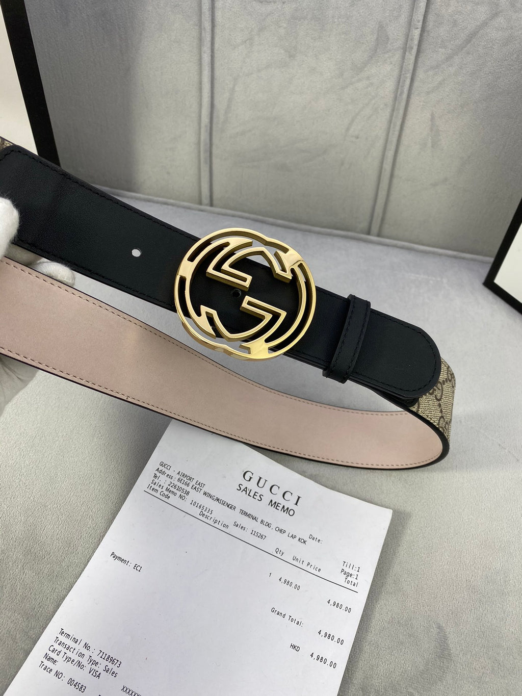 Gucci belt with gold-tone interlocking G buckle and black leather strap over tan canvas.