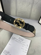 Gucci belt with gold-tone interlocking G buckle and black leather strap over tan canvas.