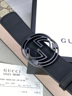 Gucci belt close-up: dark strap with round interlocking G buckle and GG monogram edge.