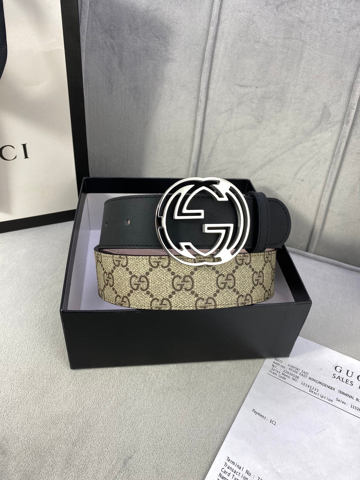 Gucci belt in box: black leather strap with interlocking G buckle and tan GG monogram panel.