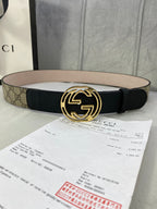 Gucci belt with black leather strap and gold-tone interlocking G buckle on tan GG canvas.