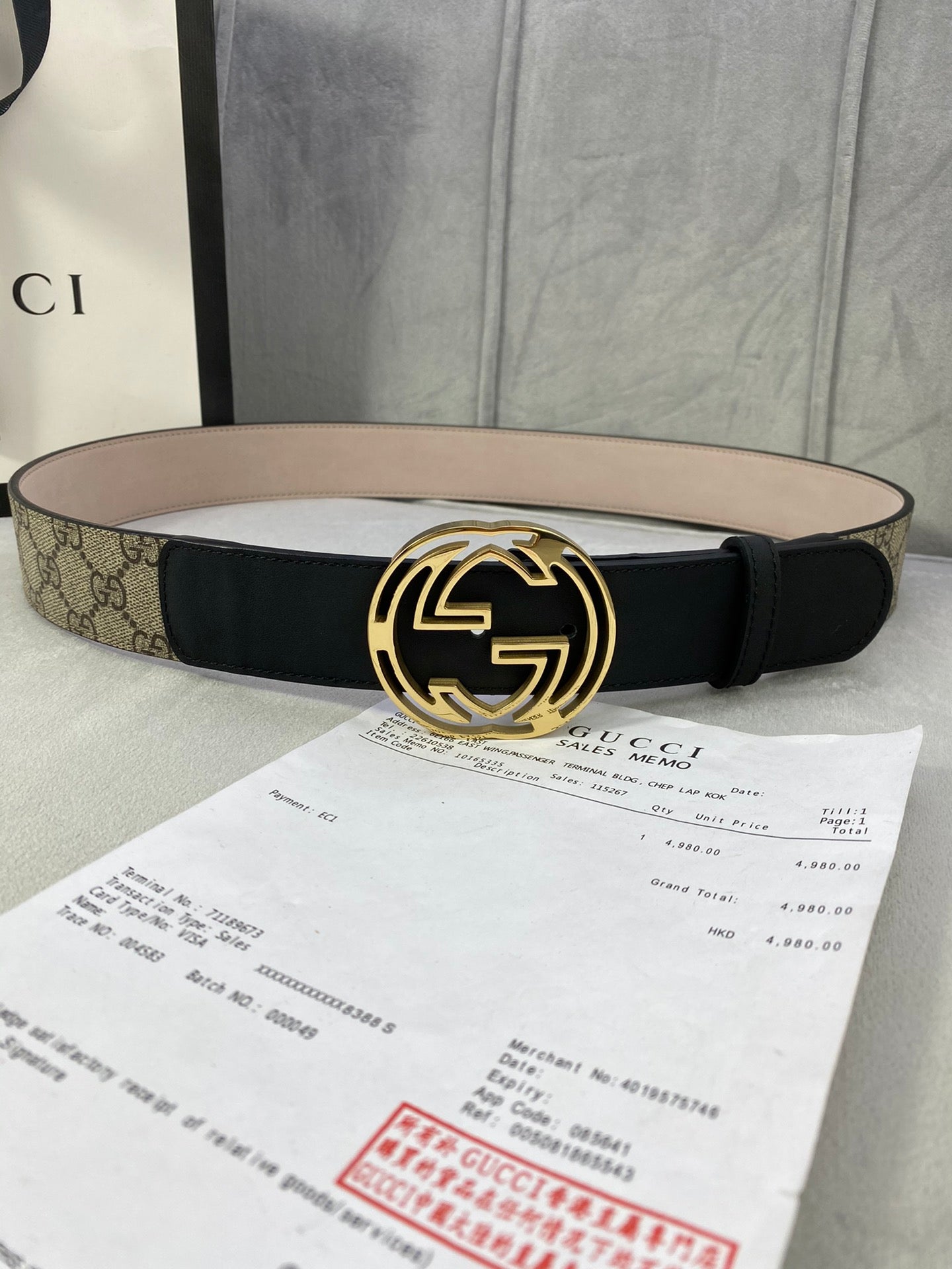 Gucci belt with black leather strap and gold-tone interlocking G buckle on tan GG canvas.