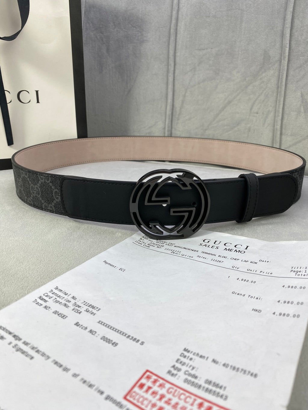 Black GG monogram belt with round silver interlocking logo buckle and tan underside.
